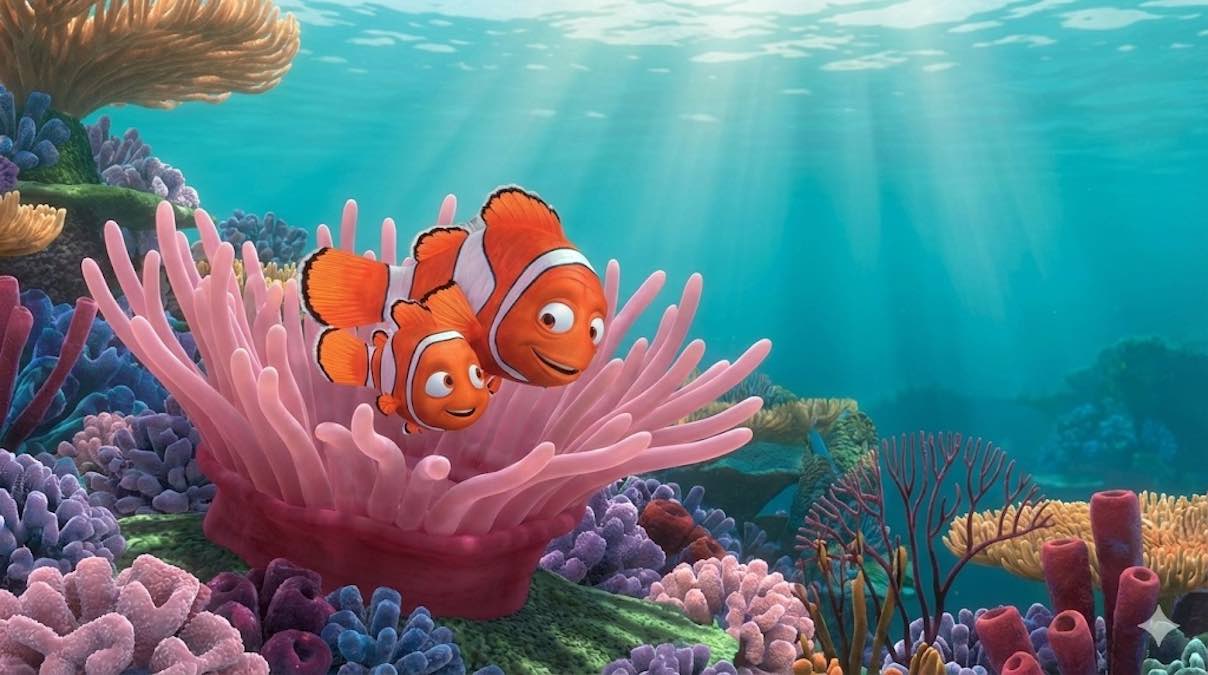 Personajes de animación Marlin y Nemo, dos peces payaso, nadando sobre una anémona rosa en un arrecife de coral bajo la luz del sol en el océano.